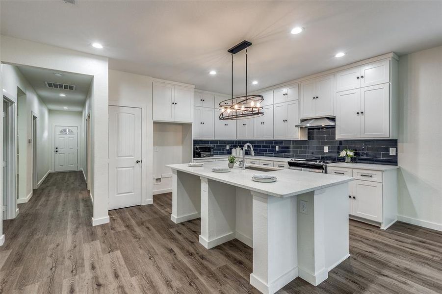 Kitchen with hardwood / wood-style floors, white cabinetry, range with two ovens, an island with sink, and pendant lighting