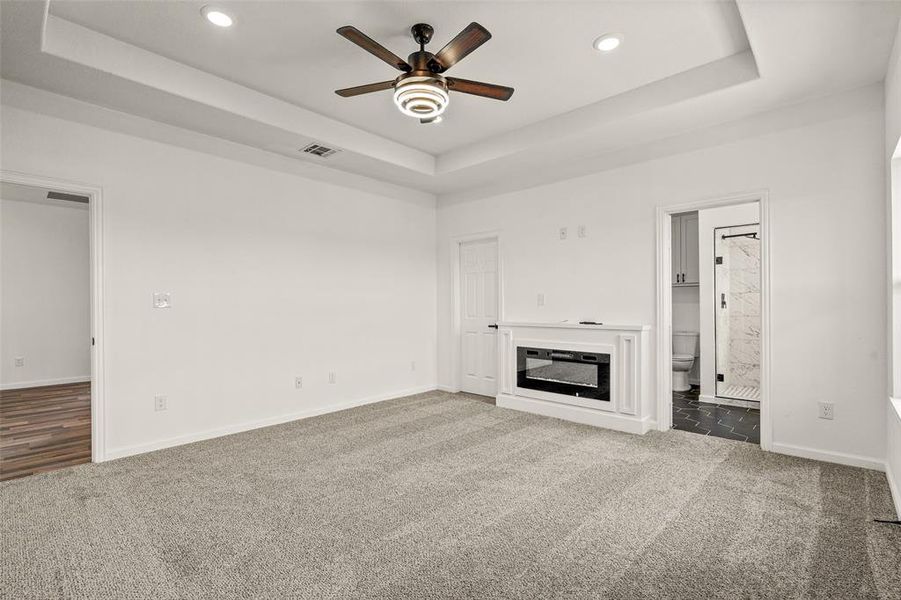 Unfurnished living room featuring a tray ceiling, carpet, and ceiling fan
