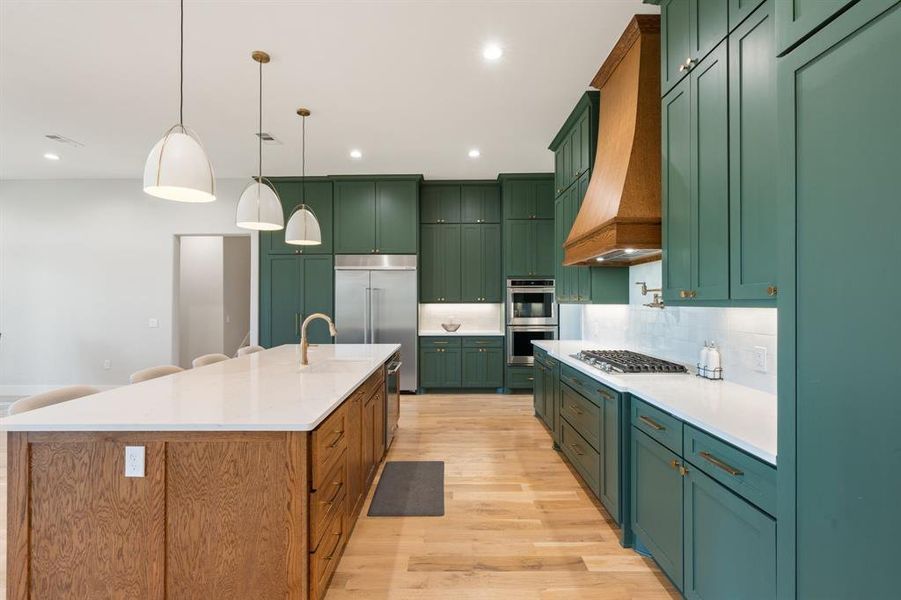 Kitchen featuring hanging light fixtures, a center island with sink, custom range hood, and light hardwood / wood-style floors