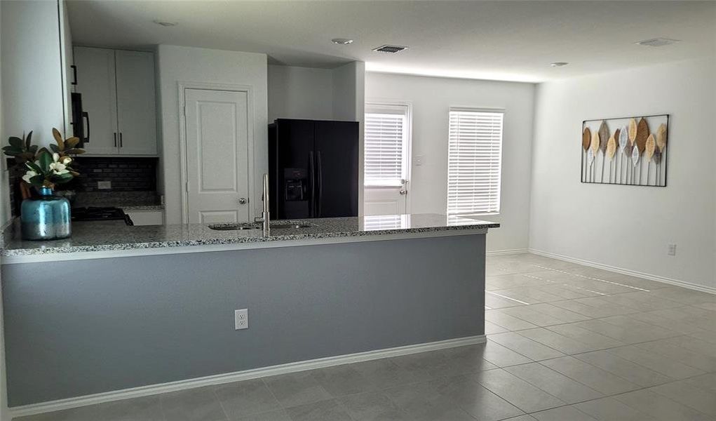 Kitchen featuring black fridge with ice dispenser, light tile flooring, kitchen peninsula, gray cabinetry, and sink