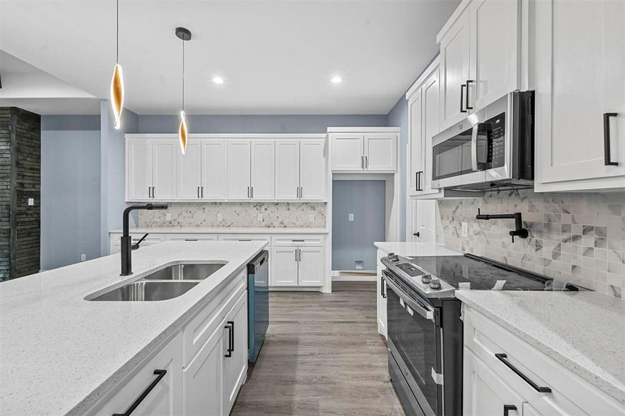 Kitchen featuring light wood-type flooring, white cabinetry, decorative light fixtures, sink, and appliances with stainless steel finishes