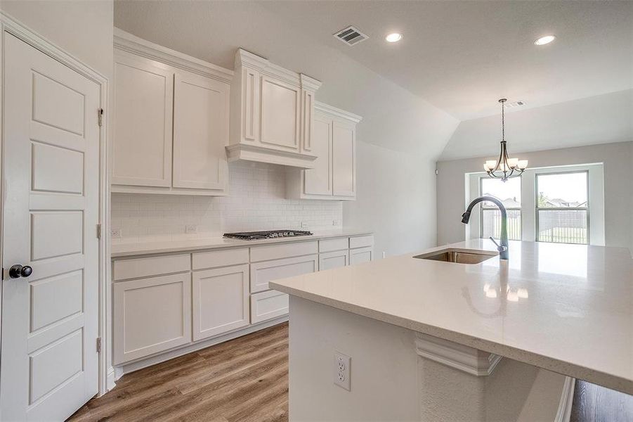 Kitchen featuring white cabinets, sink, light hardwood / wood-style floors, decorative light fixtures, and decorative backsplash