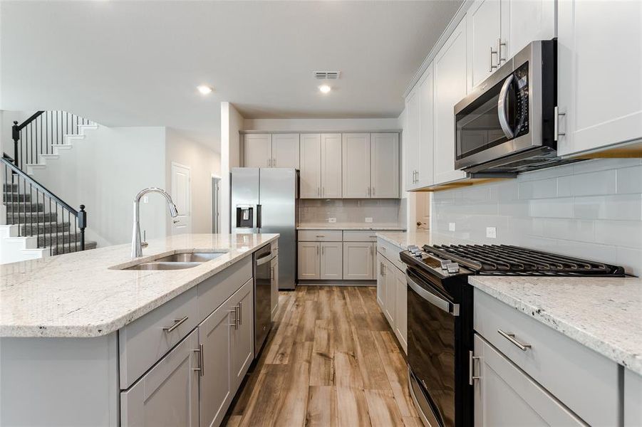 Kitchen with a center island with sink, sink, appliances with stainless steel finishes, light wood-type flooring, and decorative backsplash