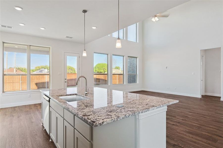 Kitchen with decorative light fixtures, light stone counters, sink, dark hardwood / wood-style floors, and a kitchen island with sink