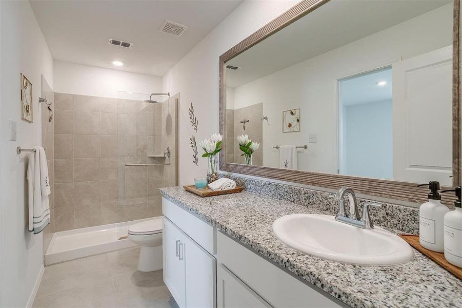 Bathroom with tiled shower, vanity, toilet, and tile floors