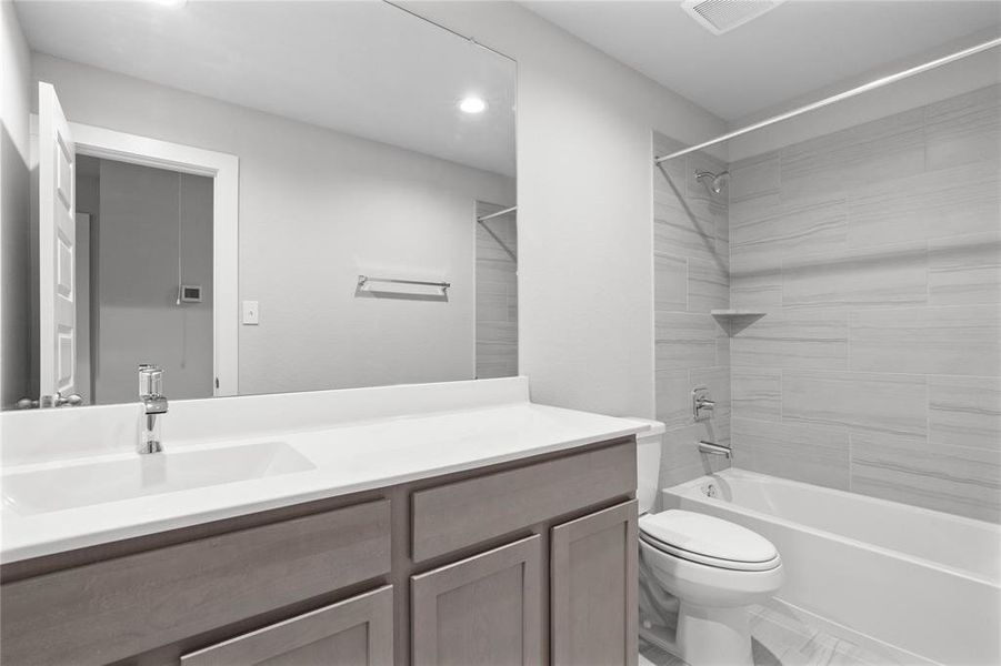 Secondary bath features tile flooring, bath/shower combo with tile surround, stained wood cabinets, beautiful light countertops, mirror, sleek fixtures and modern finishes.