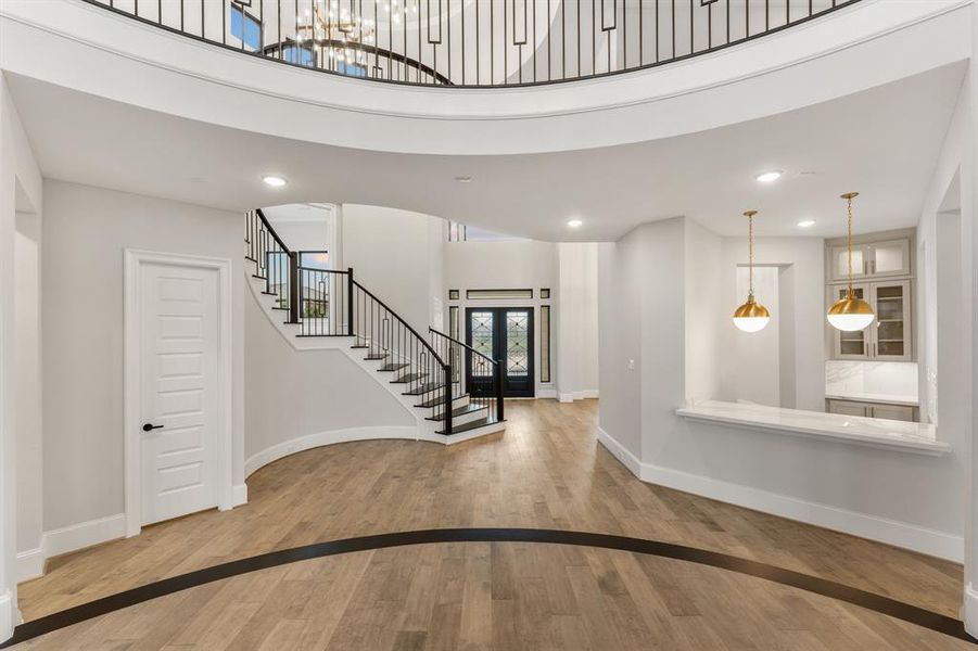 -- Representational Photo -- View from elevated 2-story living room towards the front of the home with grandiose foyer with winding staircase and butler's pantry off of formal dining room kitchen.