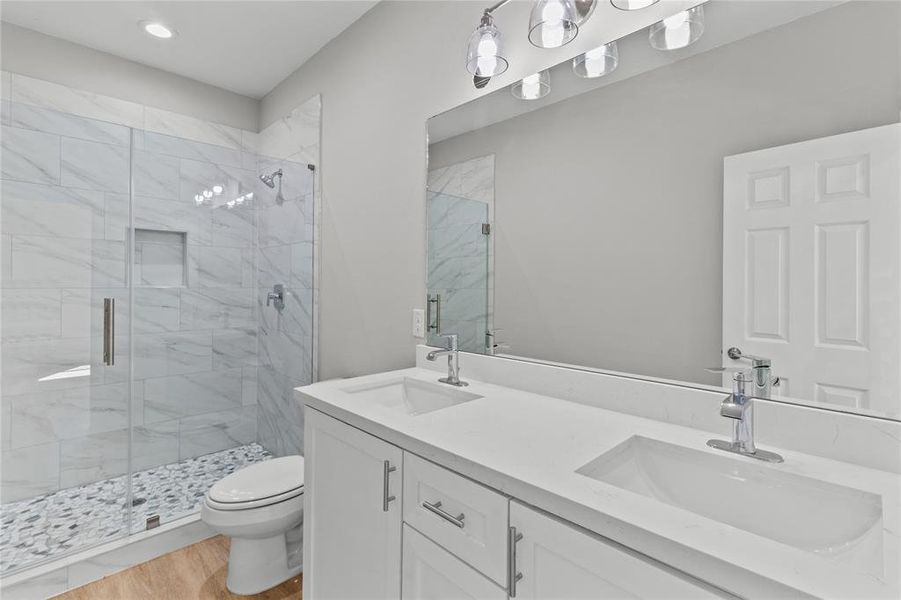 The primary bathroom is a spa-like oasis, featuring double sinks and a sleek, walk-in shower with modern glass doors.