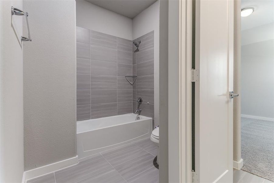 Bathroom featuring tiled shower / bath combo, toilet, and tile patterned flooring