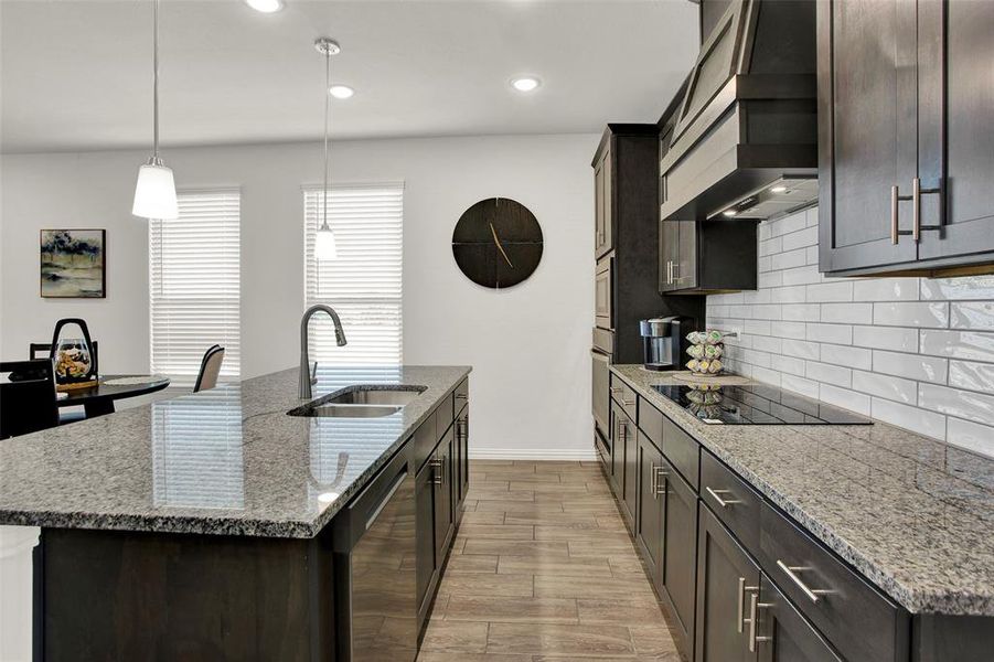 Kitchen with tasteful backsplash, stainless steel appliances, sink, custom exhaust hood, and an island with sink