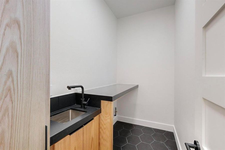 Clothes washing area with sink and dark tile patterned floors