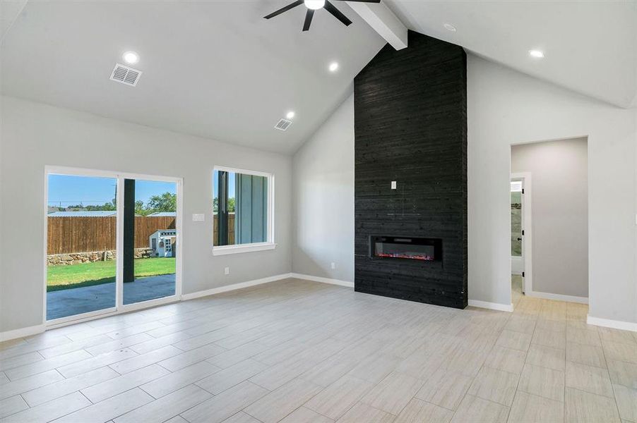 Unfurnished living room featuring ceiling fan, beamed ceiling, light hardwood / wood-style flooring, high vaulted ceiling, and a fireplace