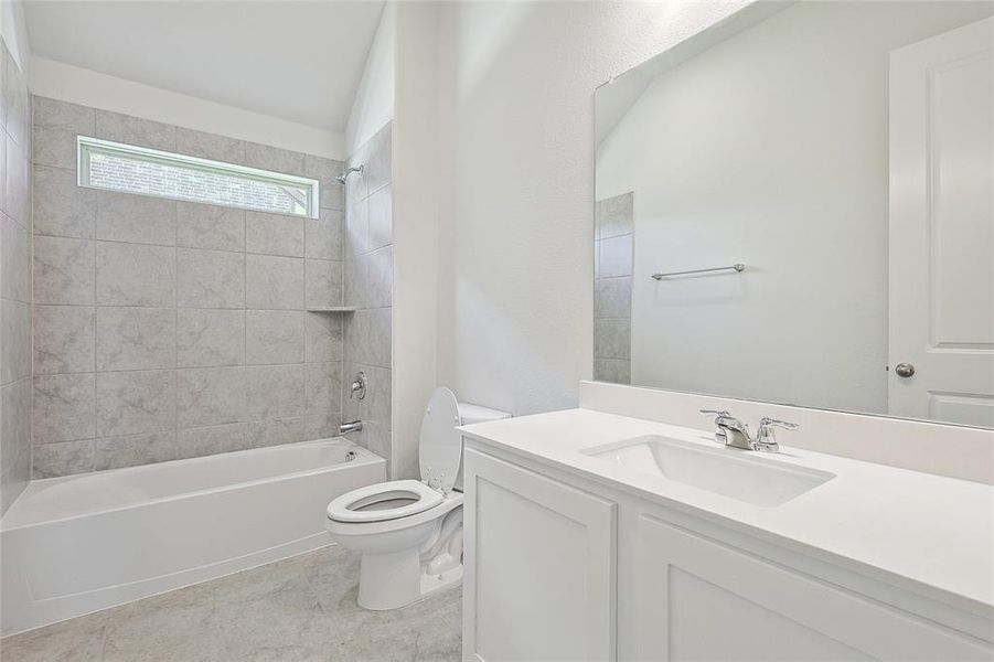 Full bathroom featuring tiled shower / bath, vanity, toilet, tile patterned floors, and vaulted ceiling