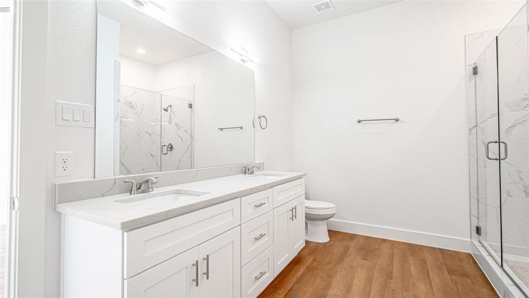 Primary bathroom with an enclosed shower, oversized vanity, hardwood / wood-style floors, toilet, and dual sinks