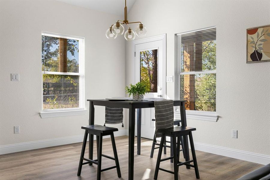 Dining space with lofted ceiling, a notable chandelier, wood-type flooring, and a healthy amount of sunlight