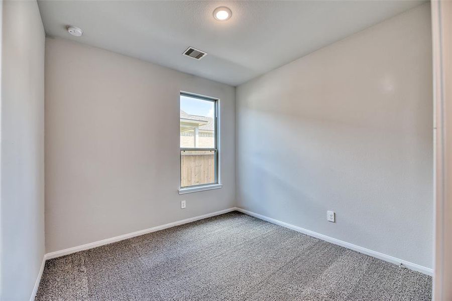 The first secondary bedroom features plush carpeting, a high ceiling with recessed lighting, and a large window that floods the room with natural light. It also includes a spacious closet, providing ample storage for clothing and personal items.