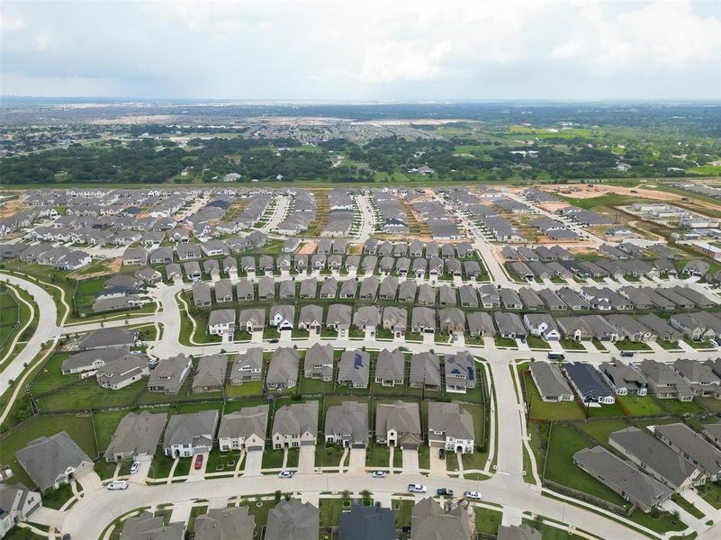 This is an aerial view of a sprawling suburban neighborhood featuring a large number of similar-style, single-family homes with well-maintained lawns and an organized street layout. The community appears relatively new with some ongoing construction, offering a modern living environment.