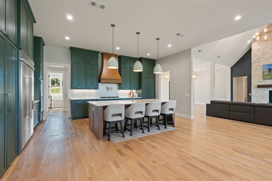 Kitchen with a center island with sink, light hardwood / wood-style flooring, premium range hood, backsplash, and a breakfast bar