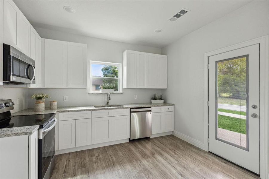 Kitchen with light hardwood / wood-style flooring, white cabinets, appliances with stainless steel finishes, and sink