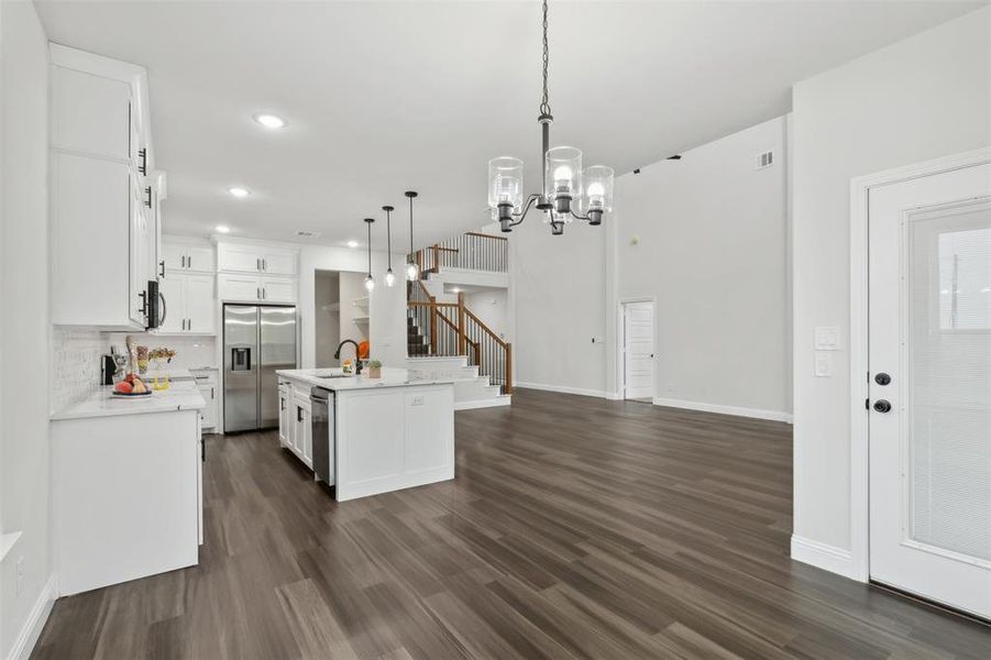 Kitchen with an island with sink, hanging light fixtures, stainless steel appliances, and white cabinetry