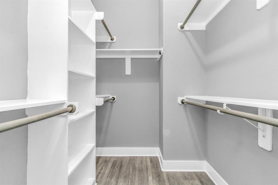 This photo shows a clean, well-lit, empty walk-in closet with built-in shelves and hanging rods, offering ample storage space for clothing and accessories.