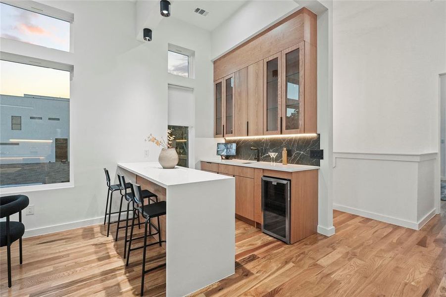 Kitchen featuring a kitchen breakfast bar, decorative backsplash, wine cooler, and light hardwood / wood-style flooring