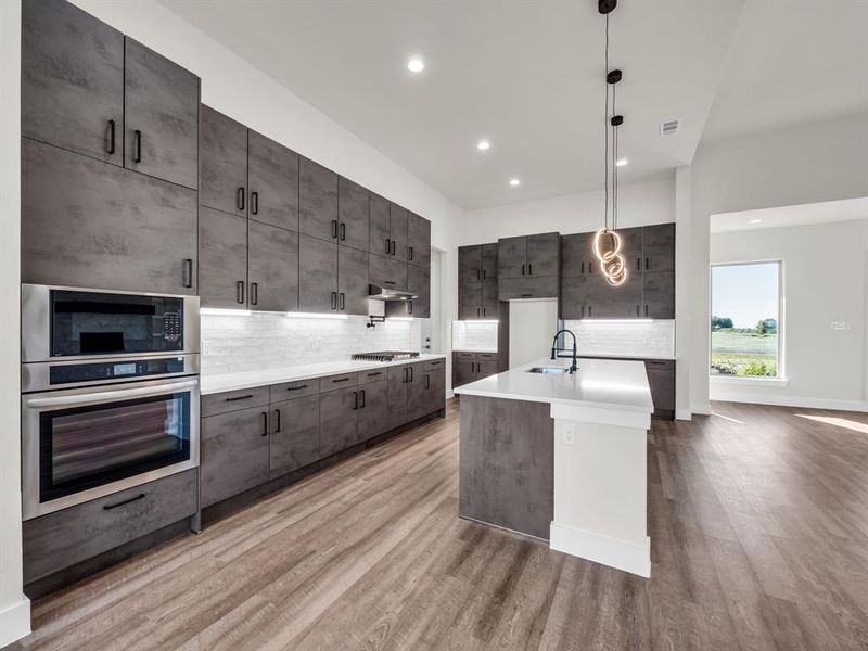 Kitchen with sink, stainless steel appliances, decorative light fixtures, light hardwood / wood-style flooring, and a kitchen island with sink