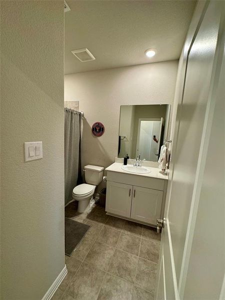 Bathroom featuring toilet, tile patterned flooring, vanity, a textured ceiling, and curtained shower