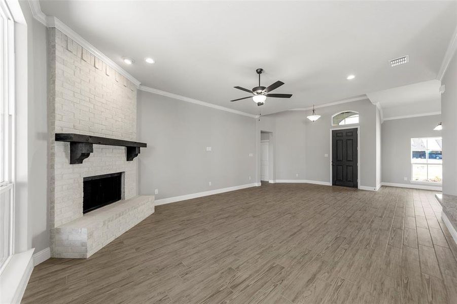 Unfurnished living room with crown molding, a brick fireplace, hardwood / wood-style flooring, and ceiling fan