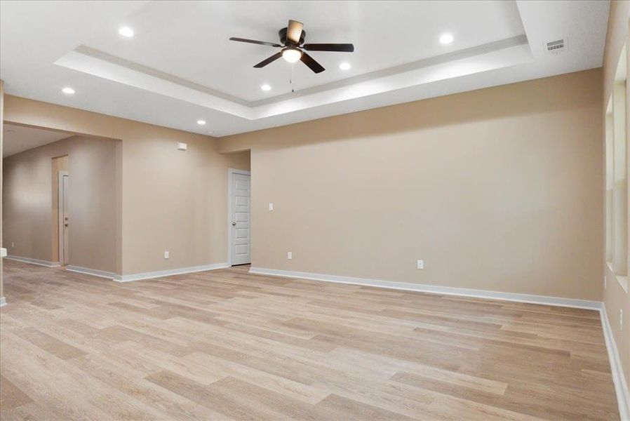 Unfurnished room featuring a tray ceiling, ceiling fan, and light hardwood / wood-style flooring