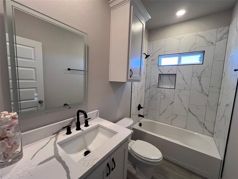 Full bathroom with wood-type flooring, tiled shower / bath combo, vanity, and toilet