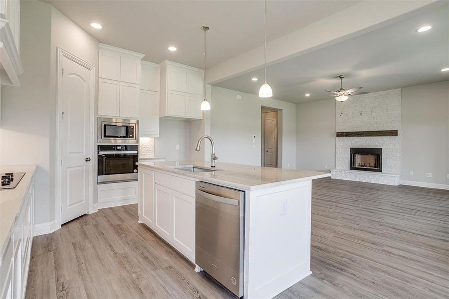 Kitchen with light hardwood / wood-style flooring, stainless steel appliances, a stone fireplace, sink, and white cabinetry