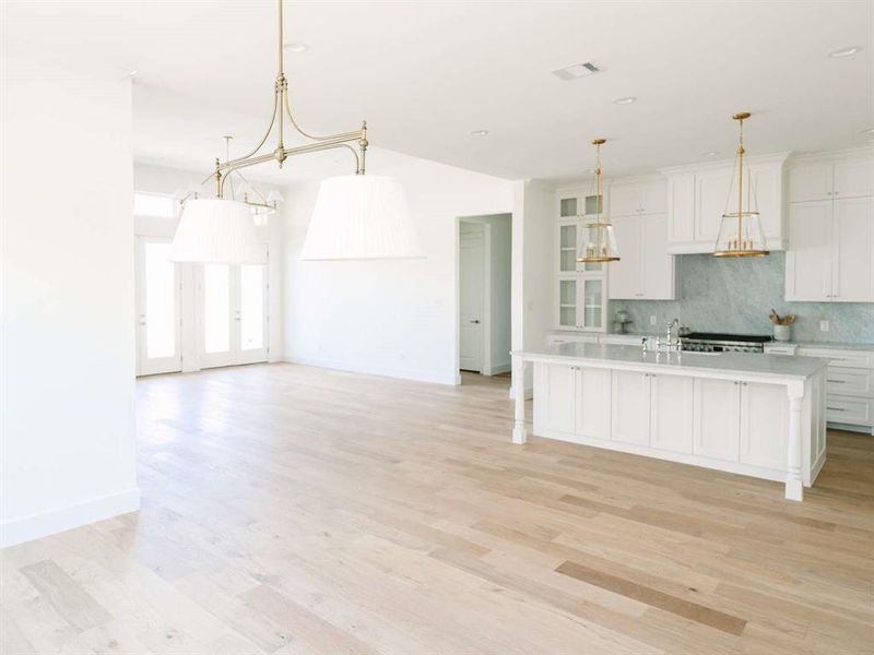 Kitchen with hanging light fixtures, a center island with sink, white cabinetry, and light hardwood / wood-style flooring