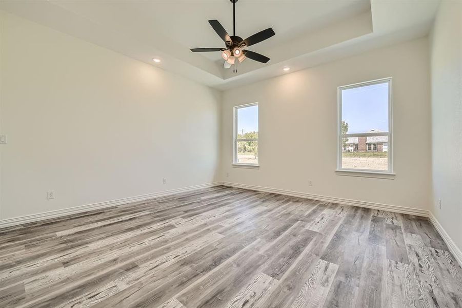 Empty room featuring ceiling fan, light hardwood / wood-style flooring, and a raised ceiling