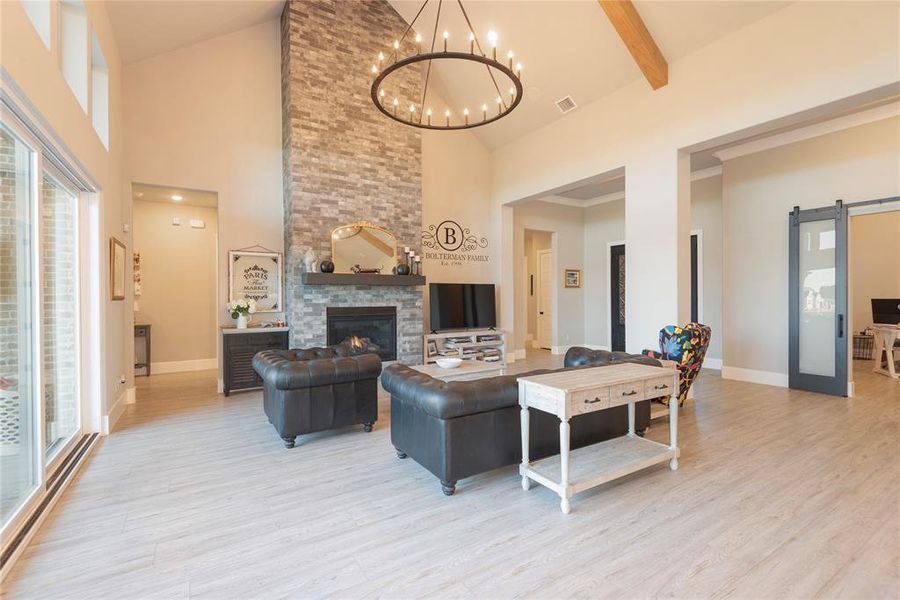 Living room featuring high vaulted ceiling, a stone fireplace, light hardwood / wood-style floors, and a barn door