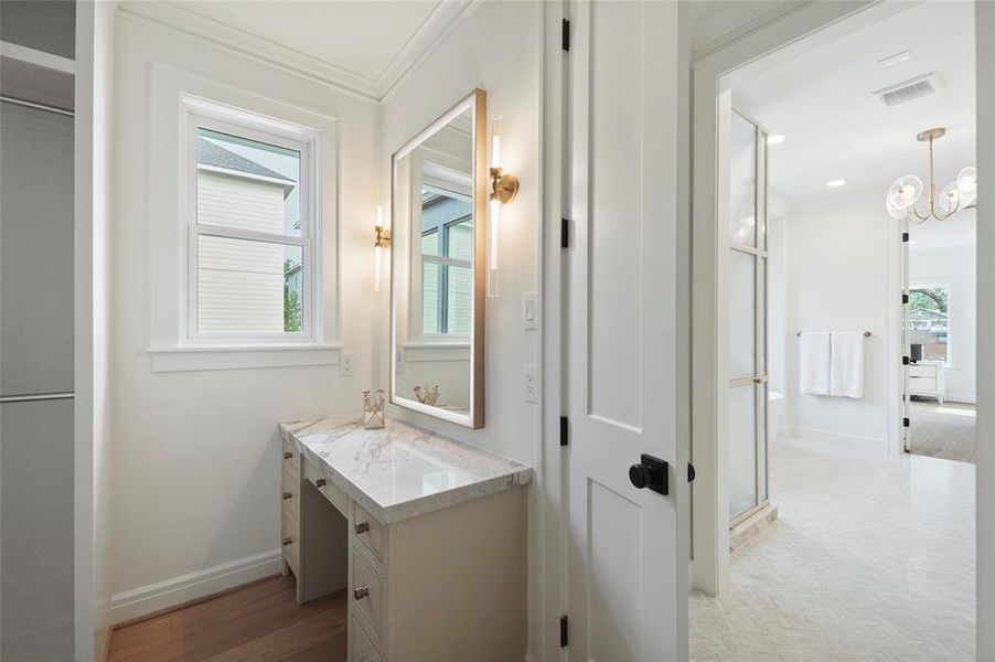 Vanity in the primary suite closet with a marble countertop, large mirror, cabinets, elegant wall sconces, and wooden flooring. Contemporary and stylish.