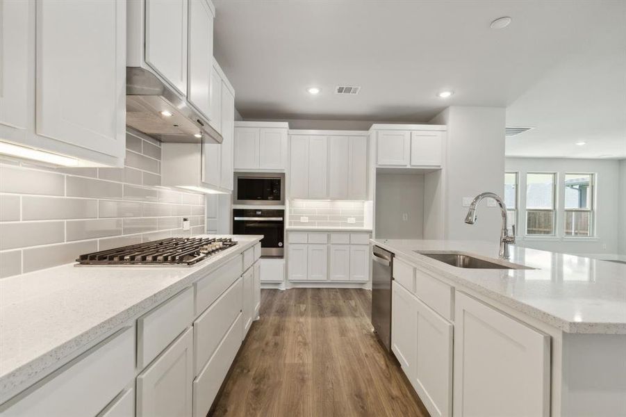 Kitchen featuring dark wood-type flooring, appliances with stainless steel finishes, light stone countertops, and sink