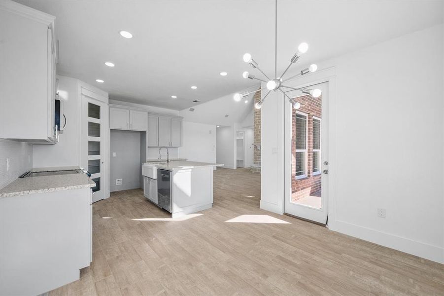 Kitchen featuring a notable chandelier, light wood-type flooring, a kitchen island with sink, stainless steel dishwasher, and vaulted ceiling