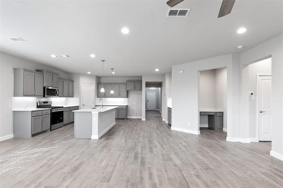 Kitchen with light hardwood / wood-style flooring, a center island with sink, decorative light fixtures, appliances with stainless steel finishes, and ceiling fan