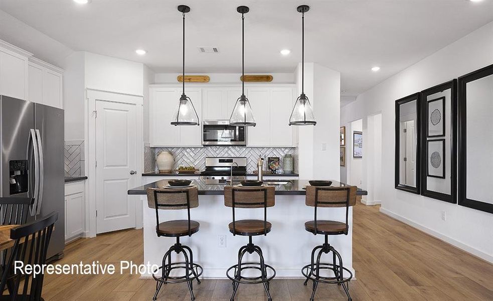 Kitchen with backsplash, stainless steel appliances, light hardwood / wood-style floors, white cabinetry, and an island with sink