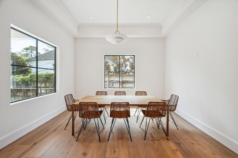 This charming breakfast room features two steel windows that overlook the wraparound covered patio, offering beautiful treetop views. Illuminated by a designer plaster chandelier and grounded by European white oak floors, the space is perfect for enjoying morning coffee in a serene setting.