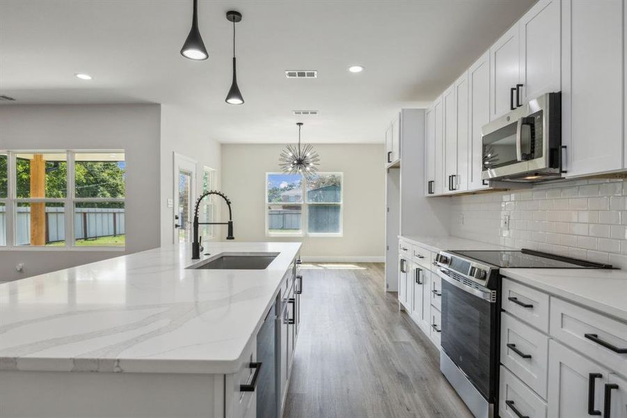 Kitchen featuring an island with sink, appliances with stainless steel finishes, plenty of natural light, and hanging light fixtures