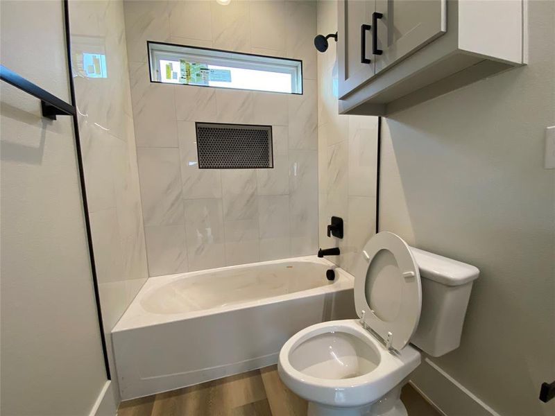 Bathroom featuring toilet, tiled shower / bath combo, and hardwood / wood-style floors