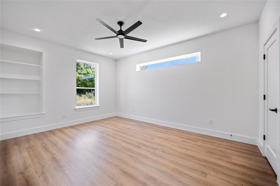 Unfurnished room with ceiling fan, built in shelves, and light hardwood / wood-style flooring
