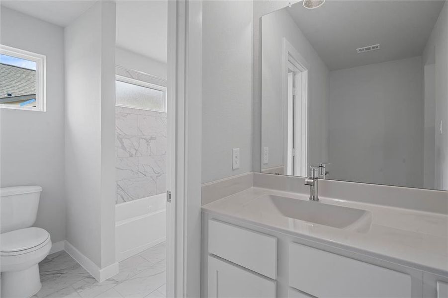 The Jack and Jill bath features tile flooring, bath/shower combo with tile surround, white stained wood cabinets, beautiful light countertops, mirror, dark, sleek fixtures and modern finishes.