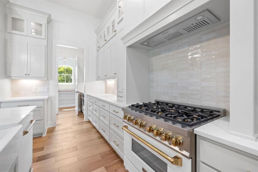 Kitchen with custom exhaust hood, high end stove, decorative backsplash, and white cabinets