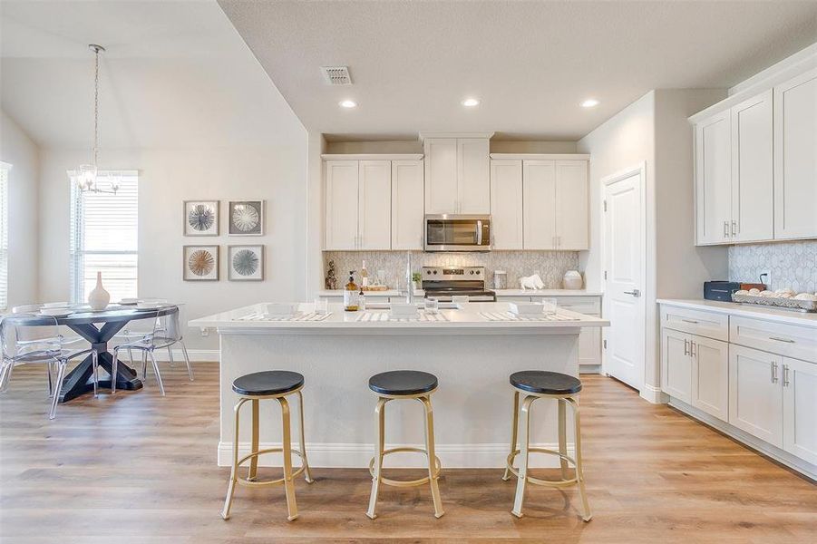 Kitchen with hanging light fixtures, light hardwood / wood-style flooring, a kitchen island with sink, white cabinetry, and appliances with stainless steel finishes