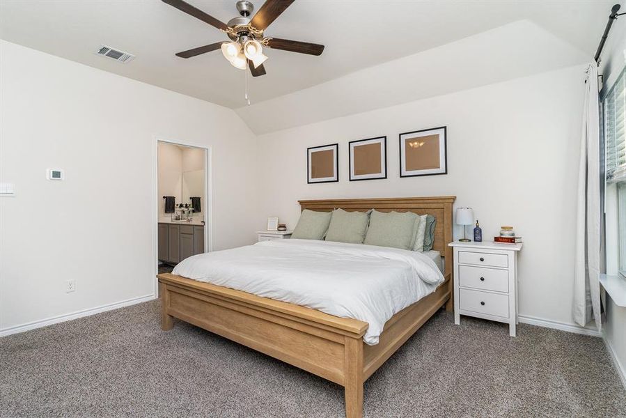 Carpeted bedroom with ceiling fan, vaulted ceiling, and ensuite bathroom