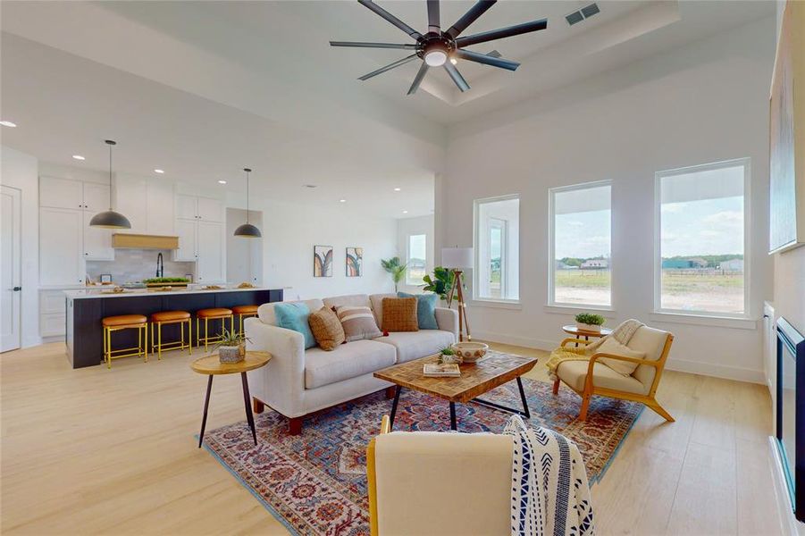 Living room with light wood-type flooring, a raised ceiling, and ceiling fan