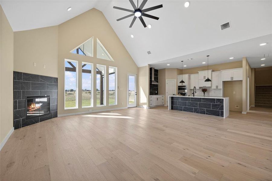 Unfurnished living room with ceiling fan, high vaulted ceiling, light wood-type flooring, a fireplace, and sink